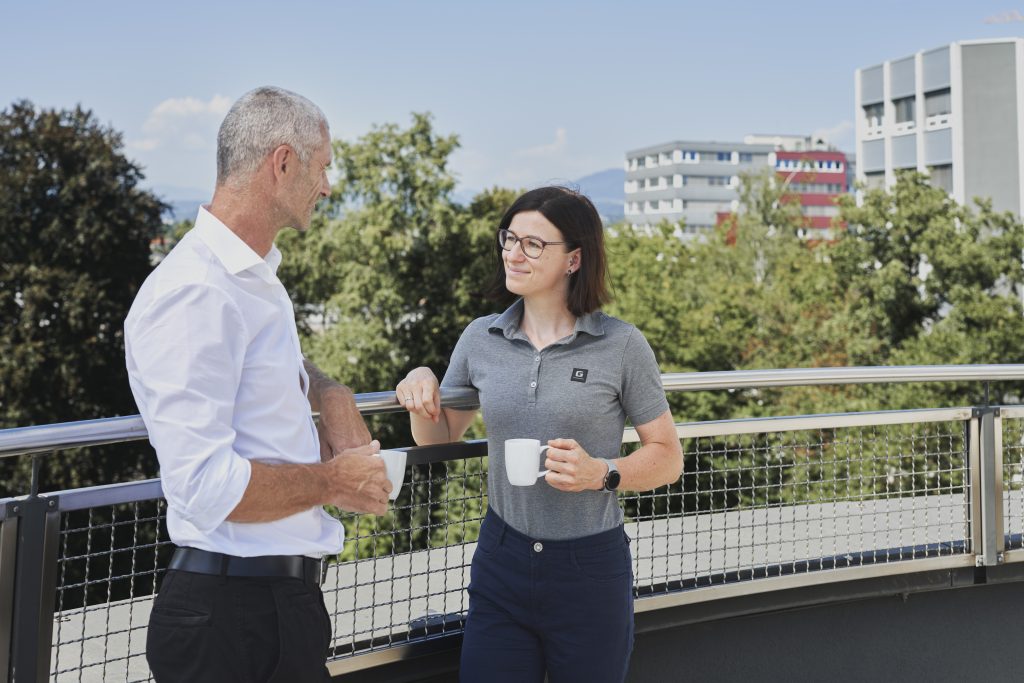 Zwei Mitarbeiter:innen der Mercedes-Benz G GmbH, die sich auf der Terrasse des Firmengebäudes unterhalten.