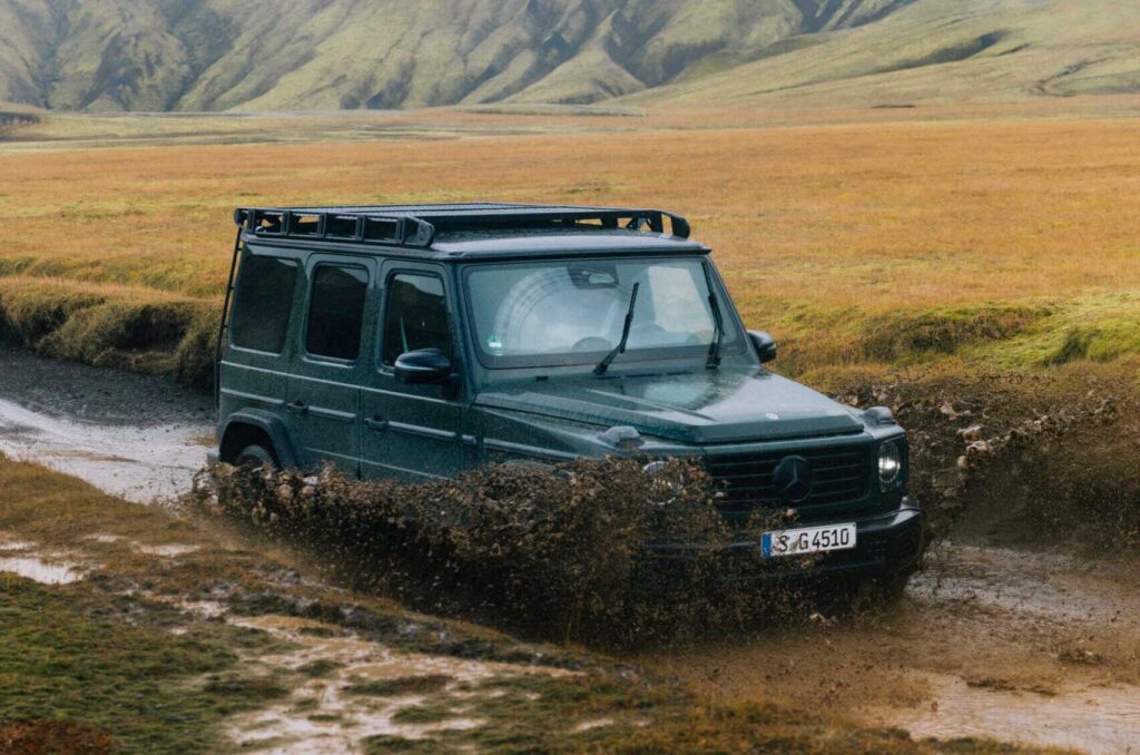 Mercedes-Benz G-Klasse durchquert eine Wasser- und Schlammstelle in einer offenen Natur- und Berglandschaft