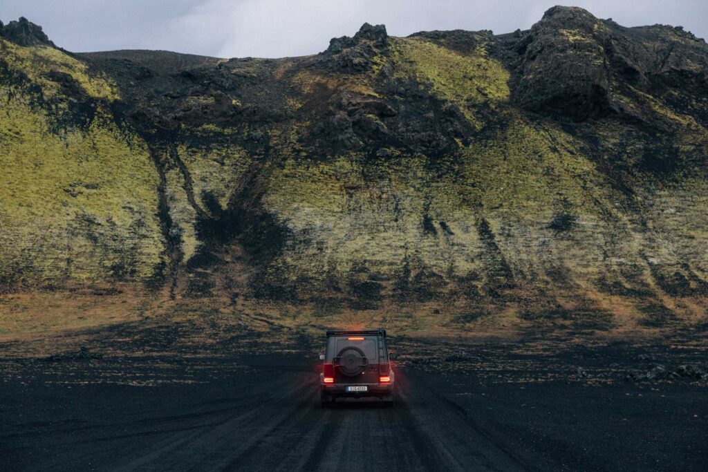 Mercedes-Benz G-Klasse fährt auf einer dunklen Sandstraße durch eine weitläufige Berglandschaft.