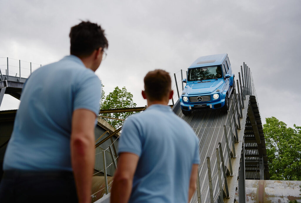 Zwei Personen sehen einer Mercedes-Benz-G-Klasse zu, wie sie extrem steil bergab fahrt.