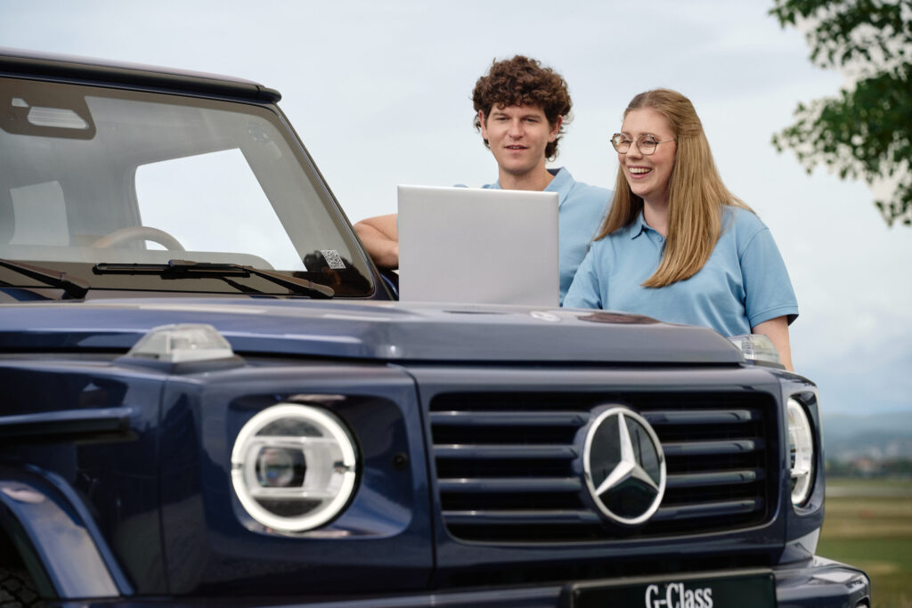 Zwei Personen stehen an einer Mercedes-Benz-G-Klasse mit einem Laptop und werten Daten aus
